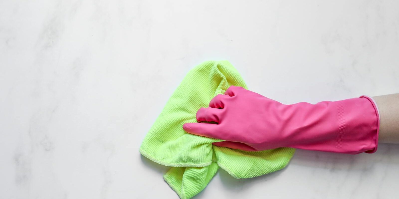 Pink rubber glove cleaning a surface with a green cloth on a white background.
