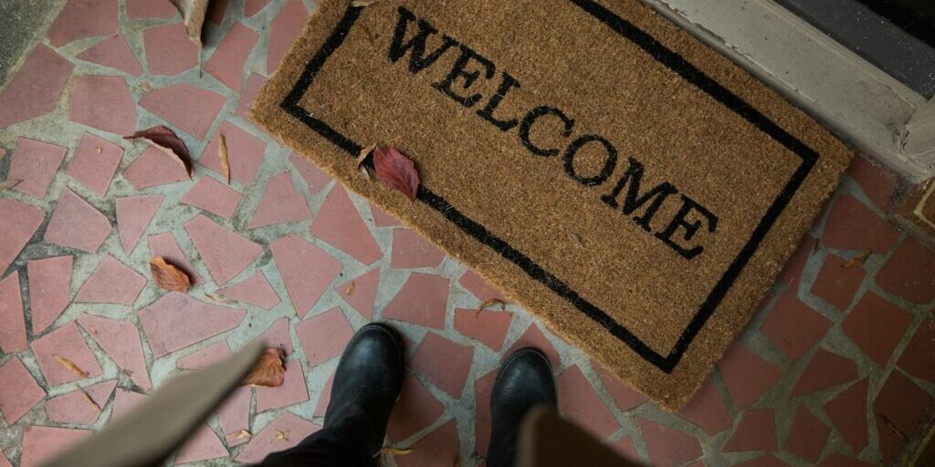Welcome mat on a tiled porch with boots visible. Perfect for home decor or hospitality themes.