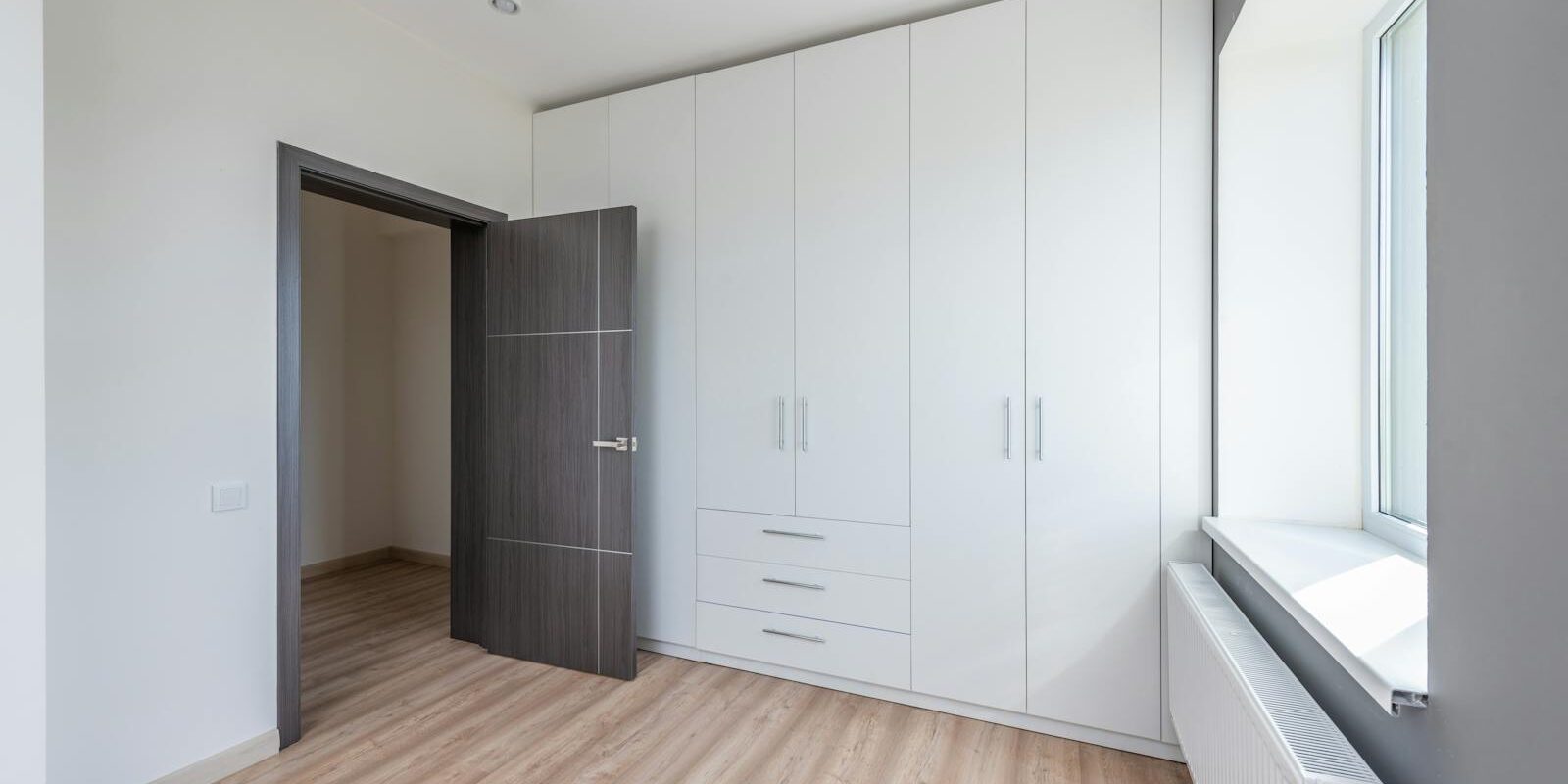 A bright, empty room featuring sleek white cabinets and wooden flooring, ideal for interior design concepts.